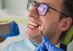 Man in black-framed glasses smiling as dentist chooses color for implant