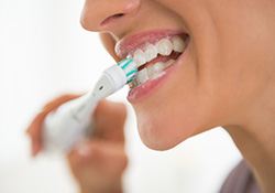 Profile nose-to-chin view of woman brushing teeth with electric brush