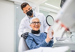 Dentist touching shoulder of woman with white hair smiling into mirror