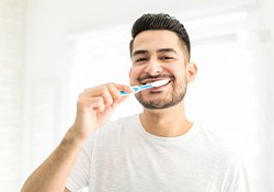 Man smiling while brushing his teeth in bathroom
