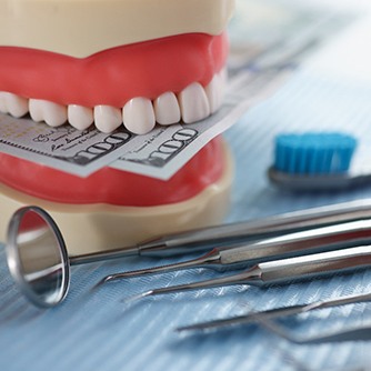 A jaw mockup holding dollar bills next to dental tools