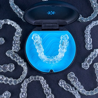 Invisalign aligners in a case surrounded by other aligners on a black background