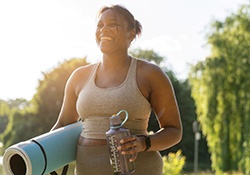 Woman with yoga mat smiling while walking in park