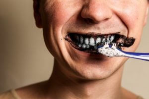 person brushing teeth with charcoal toothpaste