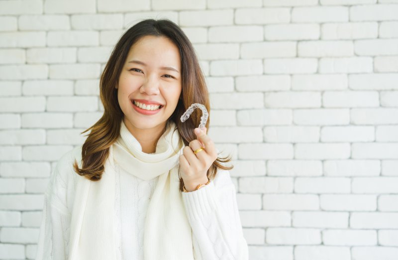 person holding clear aligner and smiling