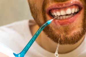 a man using a Waterpik to clean between his teeth