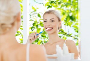 smiling woman brushing her teeth with a tree in spring in the window