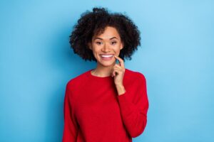 woman in a red sweater pointing to her whiter smile